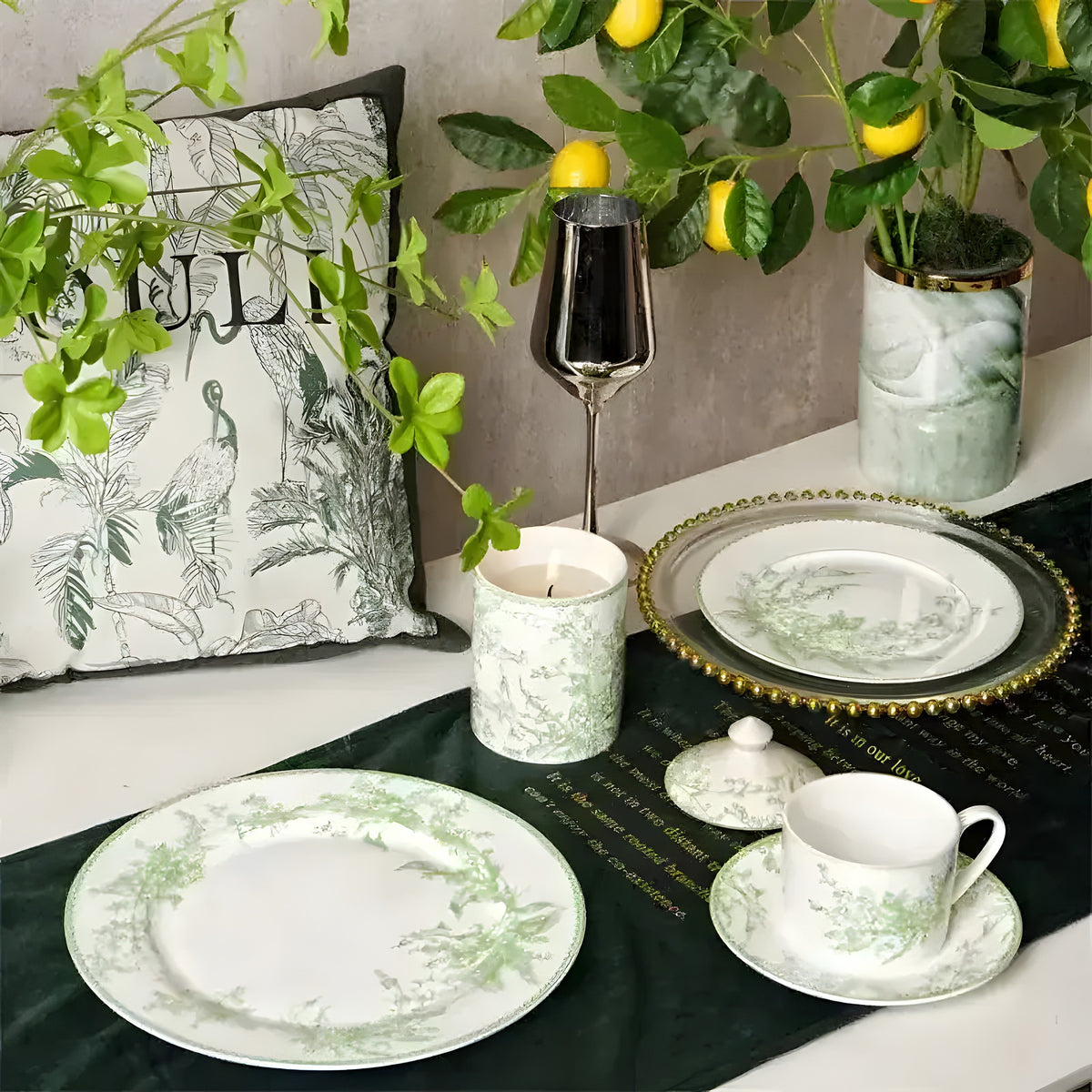 White ceramic dinnerware set with green lily of the valley botanical print, styled on dark green velvet table runner with lemon tree backdrop