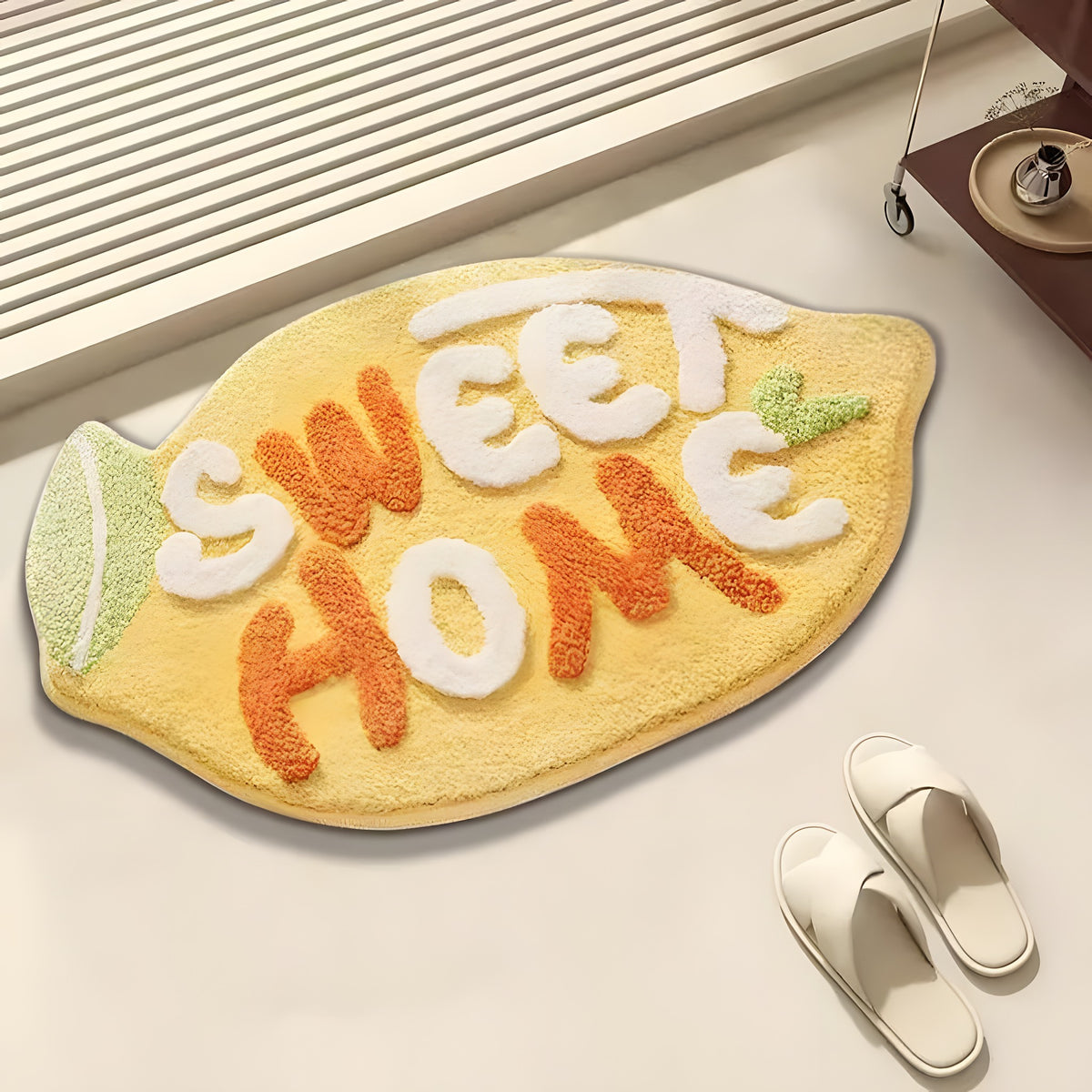 A lemon-shaped floor mat with the words 'SWEET HOME' in raised letters, styled on a light floor with white slippers nearby.