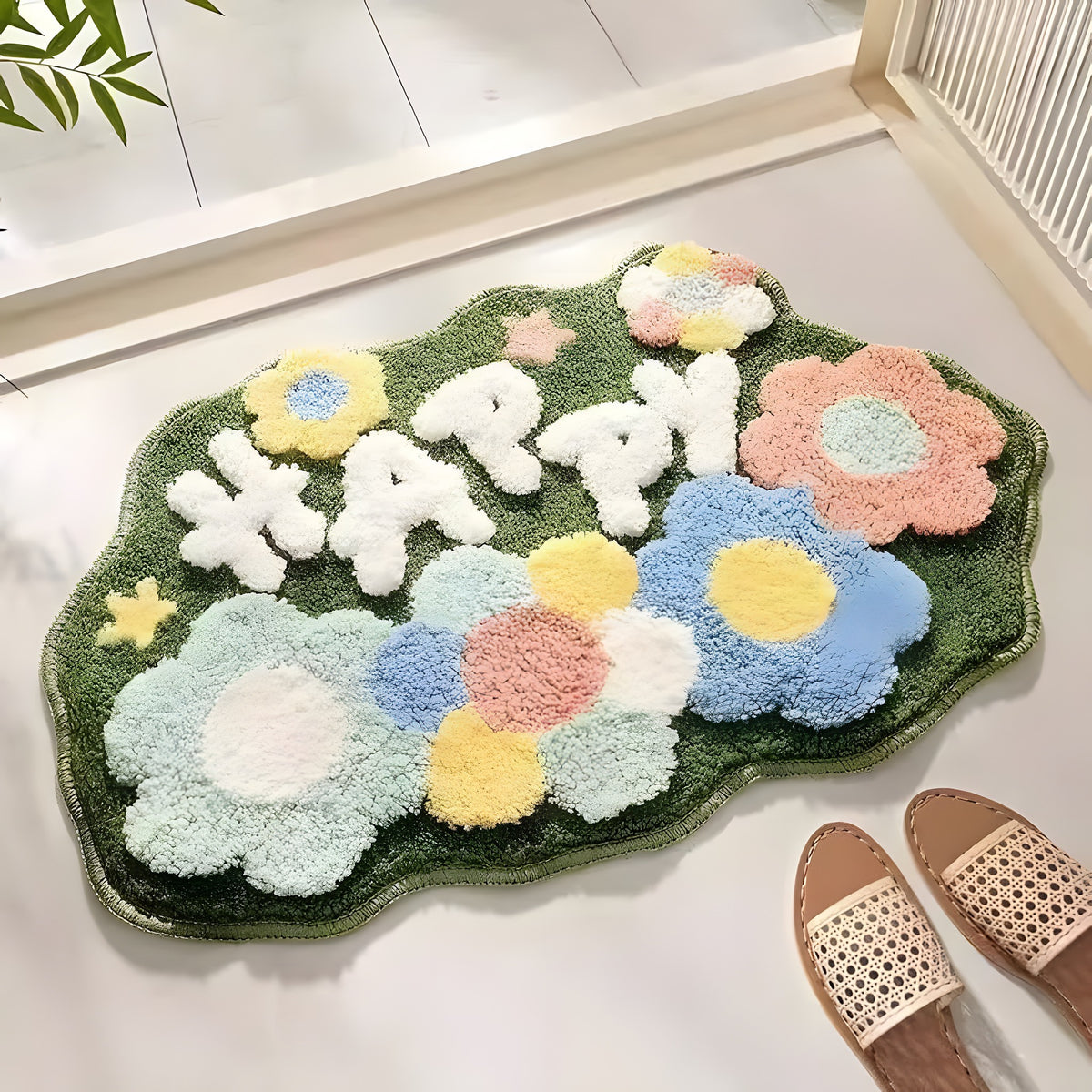 A fluffy cloud-shaped green rug with raised flowers and the word “HAPPY” in white letters, styled on a white floor with a pair of woven slide sandals nearby.