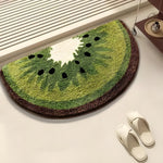 Semi-circle doormat shaped like a kiwi fruit on a light surface with white slippers nearby.