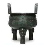 Bronze tripod cauldron with intricate designs on a wooden stand against a gray background.