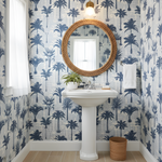 Bathroom with palm tree wallpaper, round mirror, and white sink.