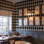 Dining area with black and white diamond patterned wallpaper and framed pictures.