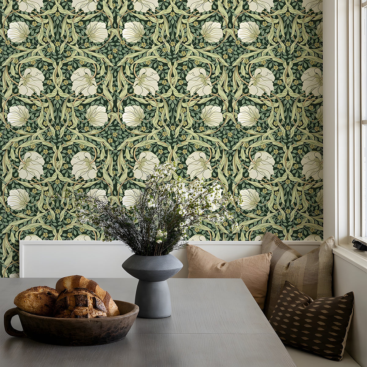 Room interior with floral-patterned wallpaper, table with bread and vase, and pillows on a bench.
