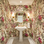 Bathroom with floral wallpaper, pedestal sink, and round mirror.