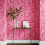 Pink wallpaper with white geometric pattern, table with decorative items against a pink wall.