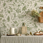 Wallpaper with green rabbits and plants on a neutral background, with a table and decorative items in the foreground.