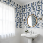 Bathroom with white pedestal sink, round mirror, and patterned wallpaper.
