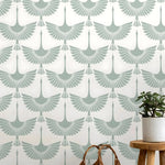 Wallpaper with crane pattern in light blue on a white background, with a plant and stool in the foreground.