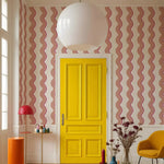 Yellow door with pink wavy-patterned walls, red lamp, and orange table in a room.