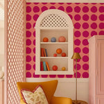 Decorative room with pink polka dot wall, white shelf with books and balls, and orange chair.