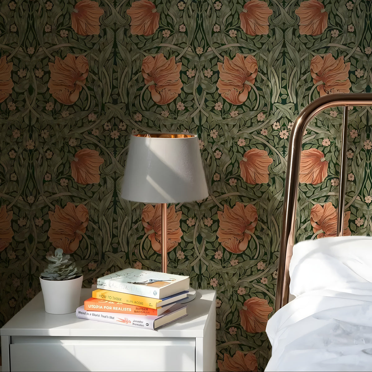 Room interior with floral wallpaper, lamp, books, and a plant on a nightstand.
