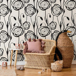 Wicker chair with pink cushion against a black and white floral wallpaper.