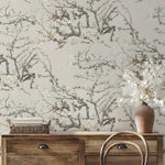 Wallpaper with floral branch design in a room with wooden furniture and decor items.
