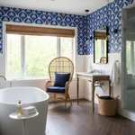 Bathroom with blue and white patterned wallpaper, white freestanding bathtub, and wooden floor.