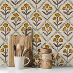 Decorative kitchen scene with wooden cutting board, mug, and decorative items against a floral wallpaper background.