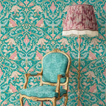 Vintage-style teal chair and lamp against a decorative wallpaper background