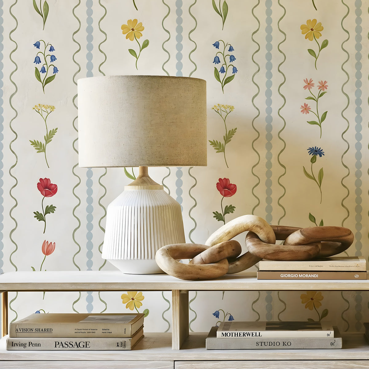 Decorative table with lamp, books, and wooden bowls against floral-patterned wallpaper.