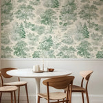 Dining area with a round table and wooden chairs against a wall with green tree-patterned wallpaper.