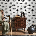 Room interior with wooden cabinet, chair, and decorative items against a wall with eye pattern.