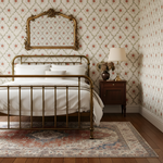 Vintage bedroom with brass bed, floral wallpaper, and wooden nightstand.