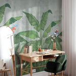 Home office with a desk against a wall featuring large green leaves and parrots.