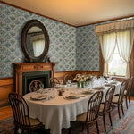 Dining room with floral wallpaper, wooden furniture, and a round table set for dinner.