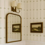 Decorative wall with mirror, framed pictures, and wall sconce against a patterned wallpaper.
