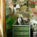 Decorative interior with a green dresser, gold mirror, and floral arrangements against a patterned wall.