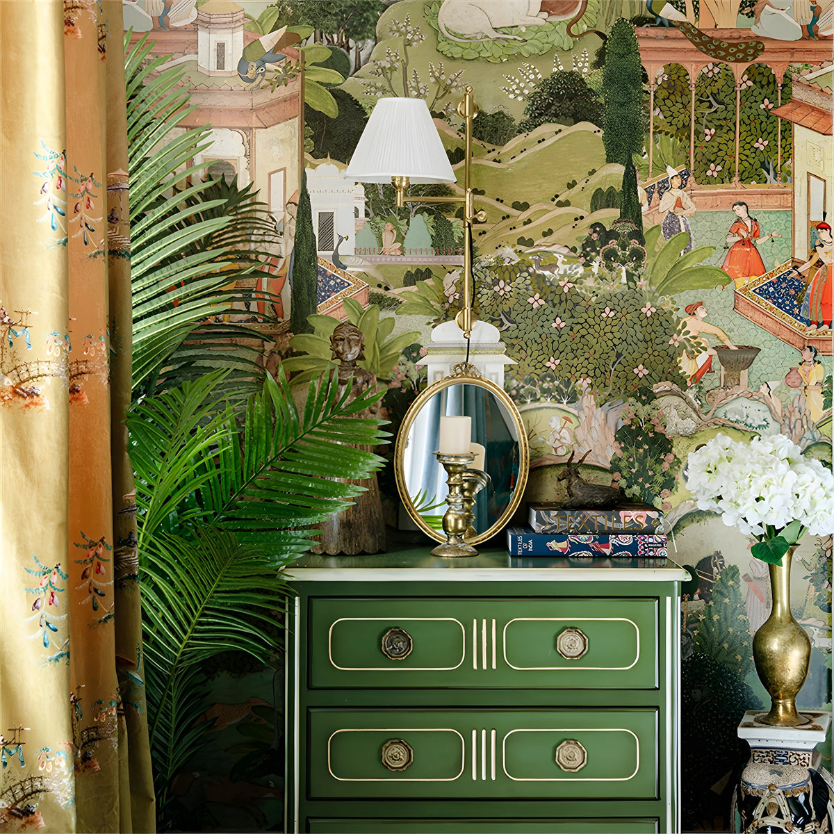 Decorative interior with a green dresser, gold mirror, and floral arrangements against a patterned wall.