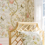 Floral wallpaper with birds and a gold headboard in a room.