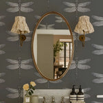 Oval mirror on a wall with dragonfly patterns and decorative lights.