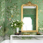 Decorative interior with floral wallpaper, gold-framed mirror, and floral arrangement.