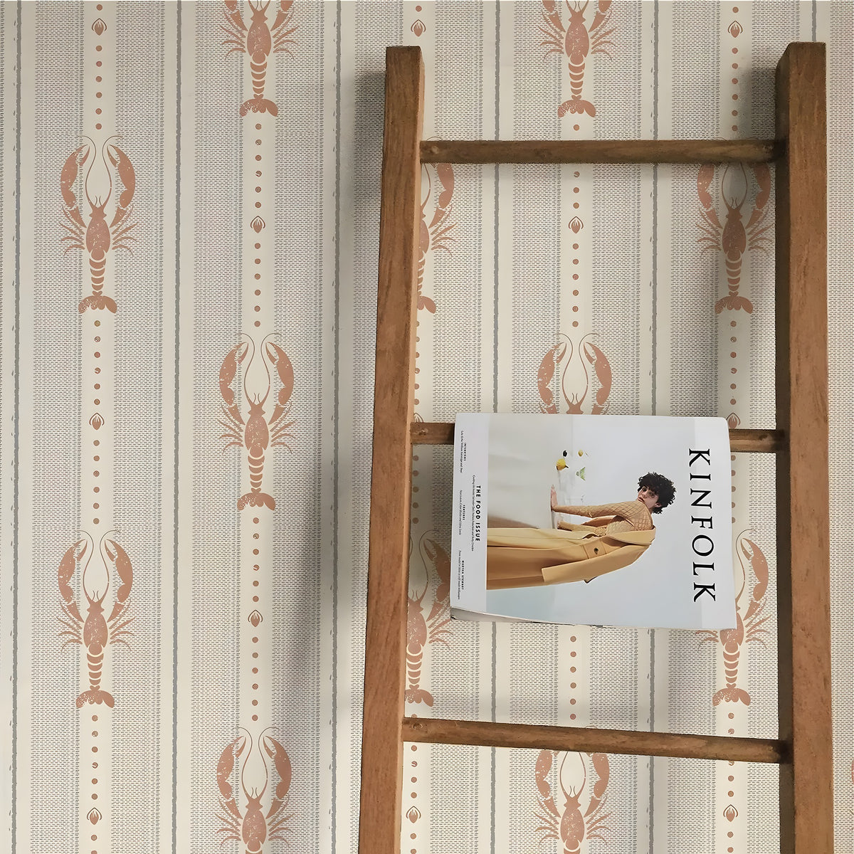 Wooden ladder with a magazine titled 'KINFOLK' against a wall with lobster patterned wallpaper.