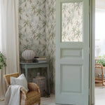 Living room with floral wallpaper, wicker chair, and open door leading to a garden.