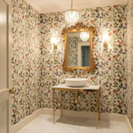 Bathroom with floral wallpaper, gold mirror, and sink.