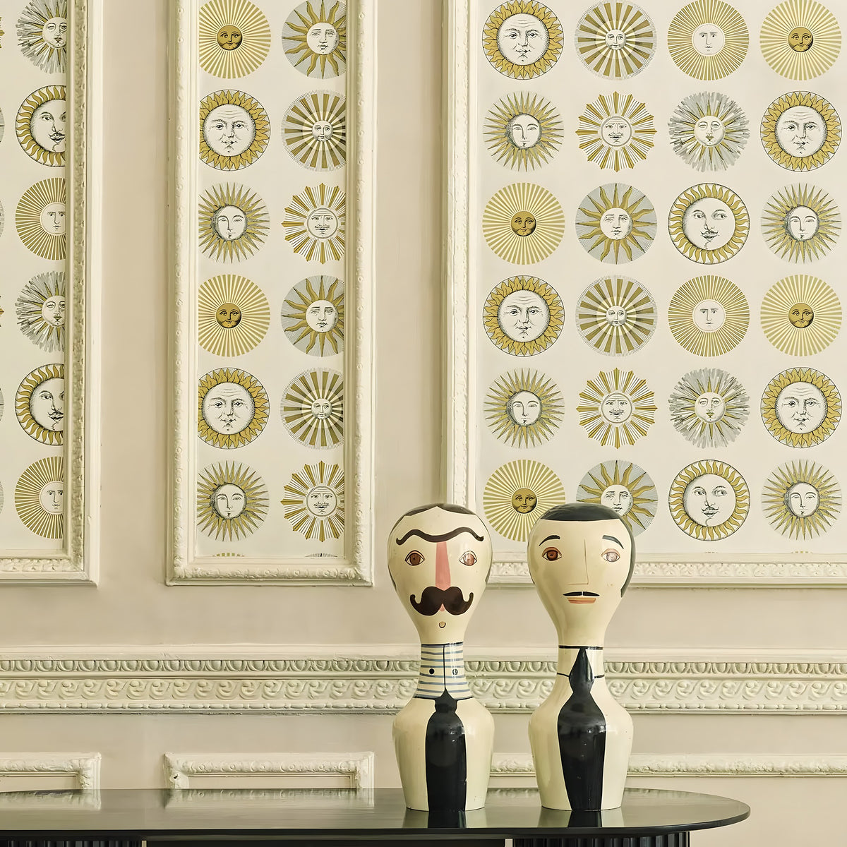 Decorative wall with sunburst pattern and two wooden figures on a table.