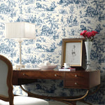 Decorative room with blue and white toile wallpaper, wooden desk, lamp, and vase.