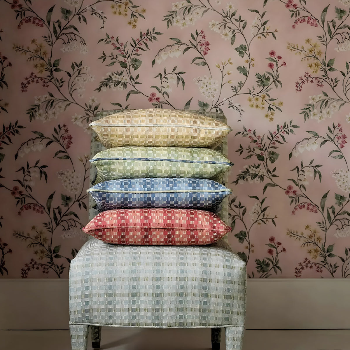 Stack of patterned cushions on a stool against a floral wallpapered wall
