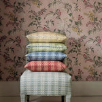 Stack of patterned cushions on a stool against a floral wallpapered wall