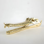 Gold-colored alligator skull on a light gray background