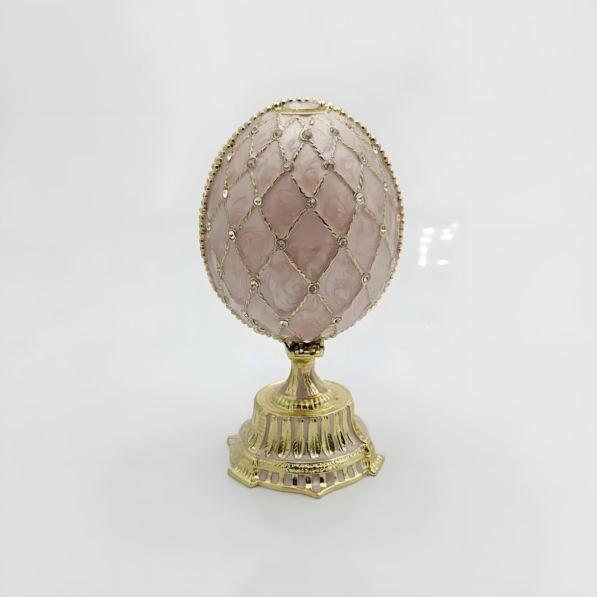 Decorative egg with pink gemstone and gold lattice design on a white background