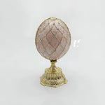 Decorative egg with pink gemstone and gold lattice design on a white background