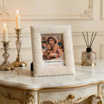 Decorative photo frame with a child holding a teddy bear on a marble table with candles and a diffuser.