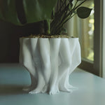 White ceramic planter shaped like legs on a light surface with a blurred background