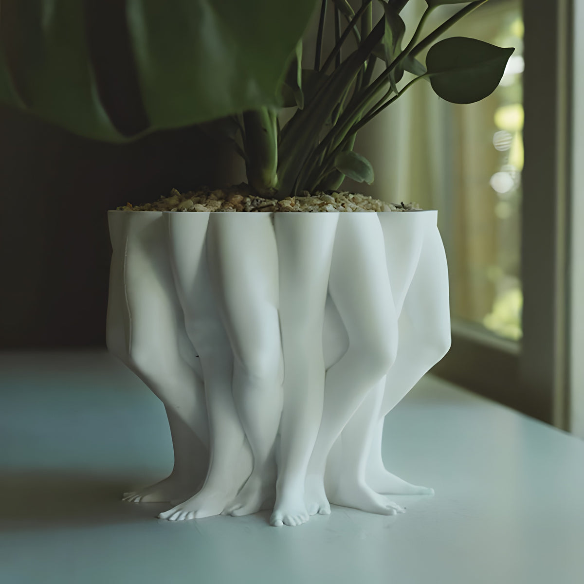 White ceramic planter shaped like legs on a light surface with a blurred background