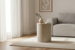 A cylindrical side table with a beige and white scallop pattern, styled in a bright, modern living room next to a light gray sofa and white curtains.