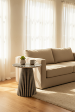 A modern beige fabric sofa in a bright living room next to a black-and-white striped side table with a small potted succulent and a mug.