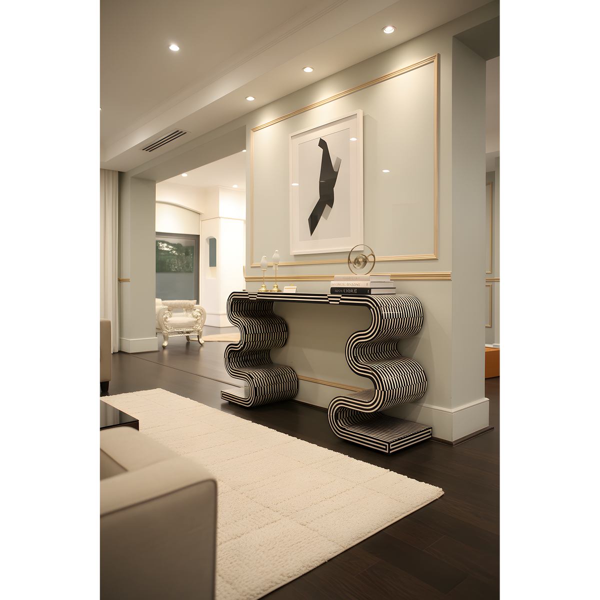 A modern living room interior featuring a sculptural black and white striped console table against a beige wall with gold trim, a large framed abstract print, a cream rug, and dark wood flooring.