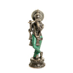 A standing metal statue of a flute-playing deity with a silver-toned finish and bright green painted accents on the draped garments, set against a plain white background.